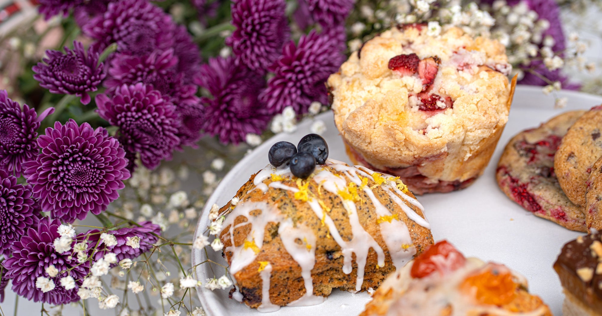 A variety of pastries sits on a platter beside flowers