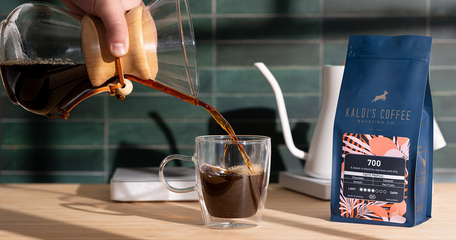 Chemex coffee maker next to two mugs, a kettle, and a 12oz bag of Cafe Kaldi
