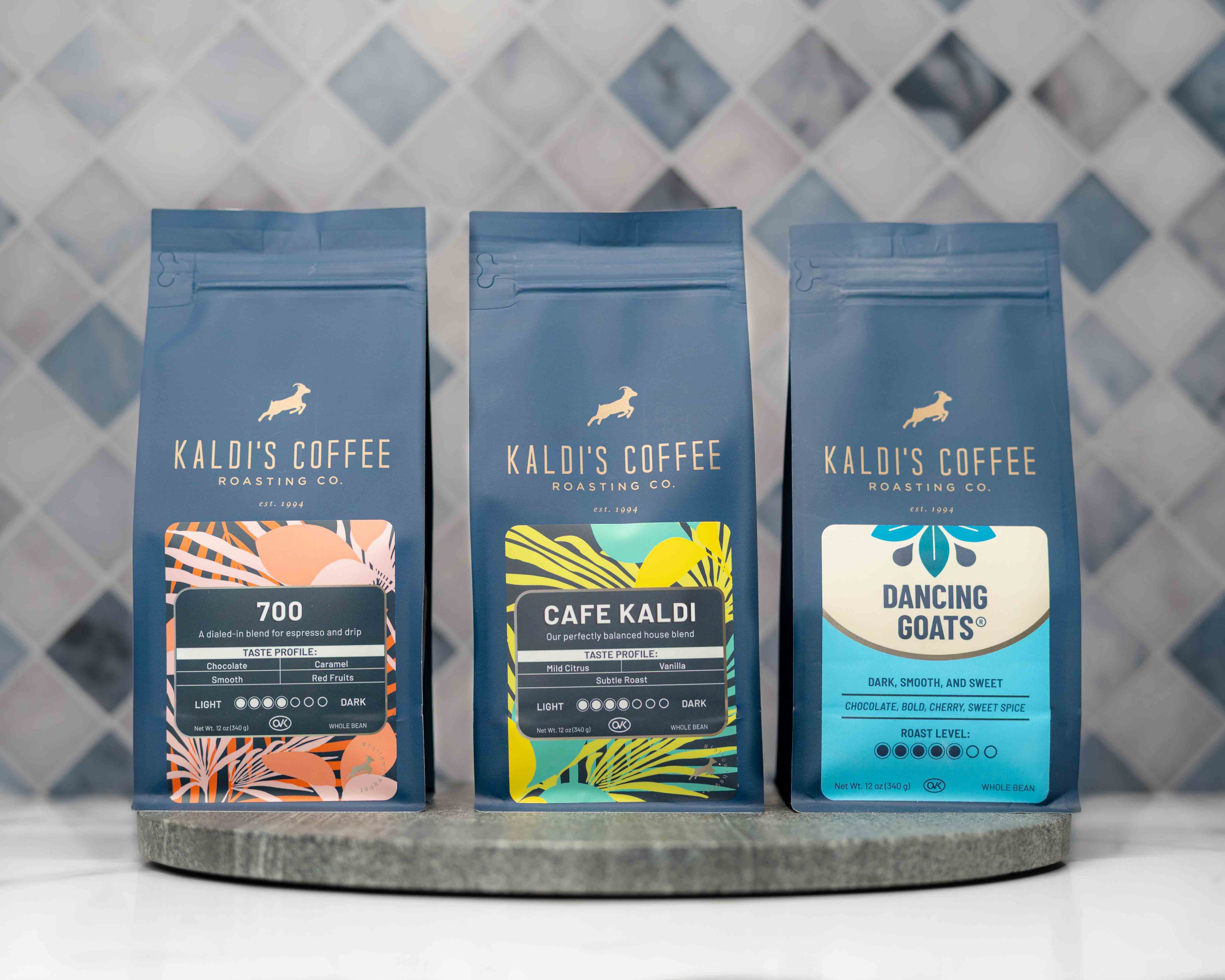Three Kaldi's Coffee packages on a round metal tray with a patterned wall background.