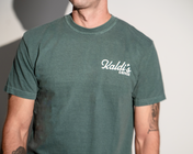 A man wearing a vintage dark green crewneck t-shirt with a white 'Kaldi's Coffee' logo.