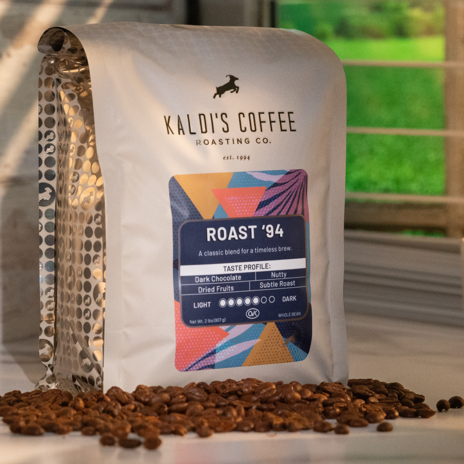 Kaldi's Coffee Roasting Co. coffee bag with roasted beans and a cup on a blurred outdoor background