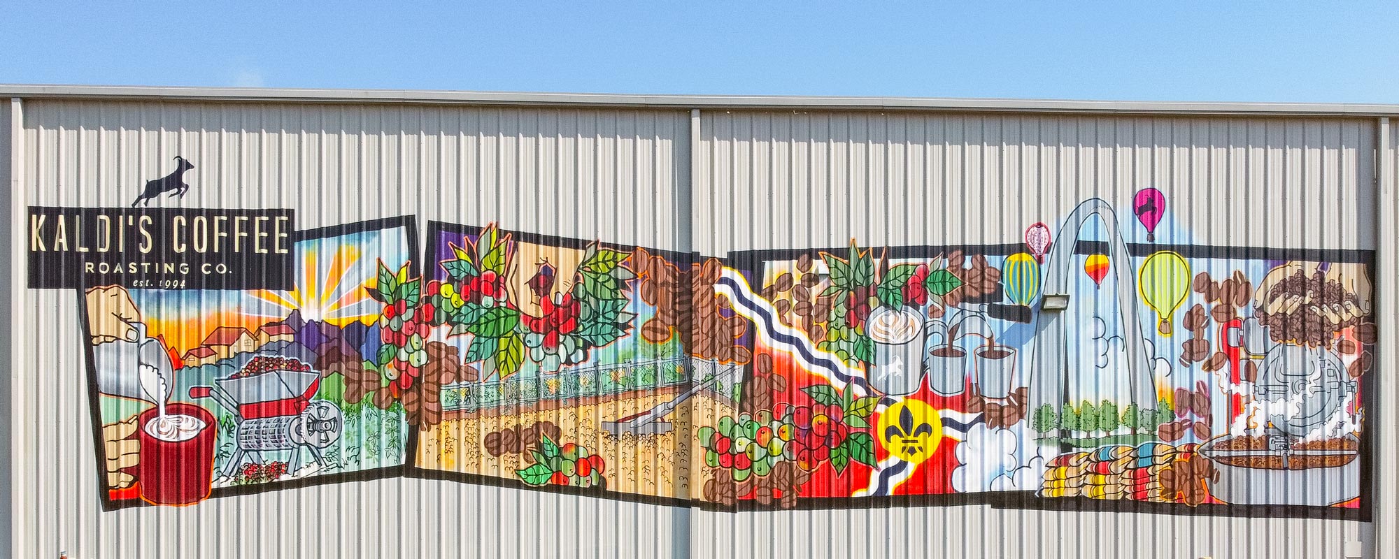 Colorful mural on a building exterior with various scenes and text "Kaldi's coffee roasting co est. 1994"